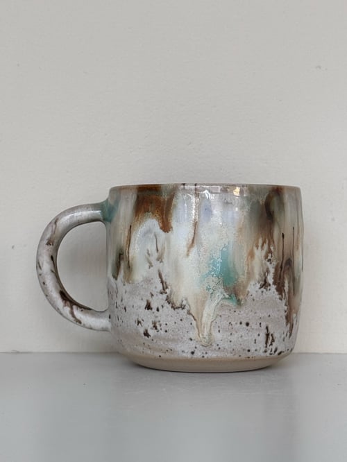 Ceramic kop med et håndlavet, abstrakt glasurdesign i jordfarver, herunder brune, hvide og blå nuancer, mod en lys baggrund. (1)