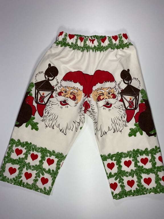 Bukser med juletema, dekoreret med motiver af julemænd iført nissehuer, lanterner, grønne grangrene og røde hjerter.