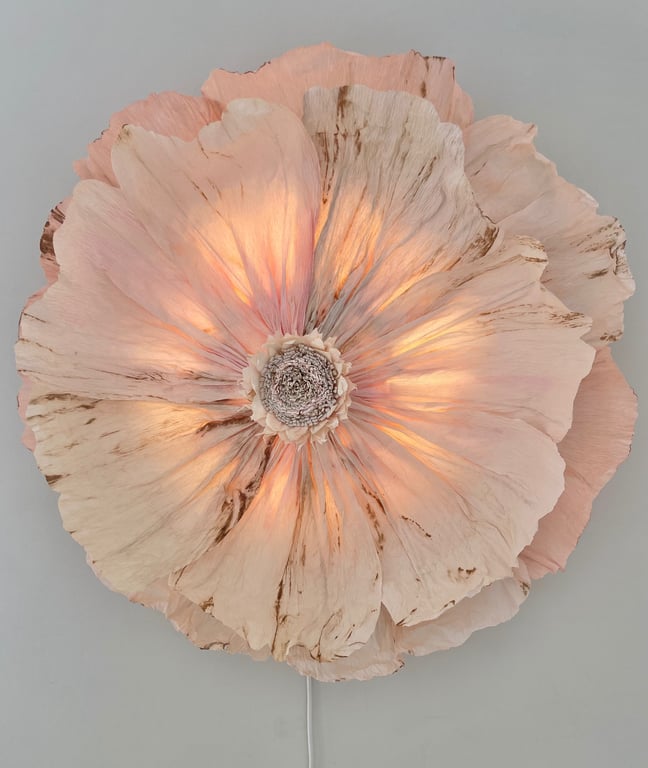 Blomstformet væglampe med lyse, lyserøde og beige kronblade, der udsender et varmt, blødt skær.