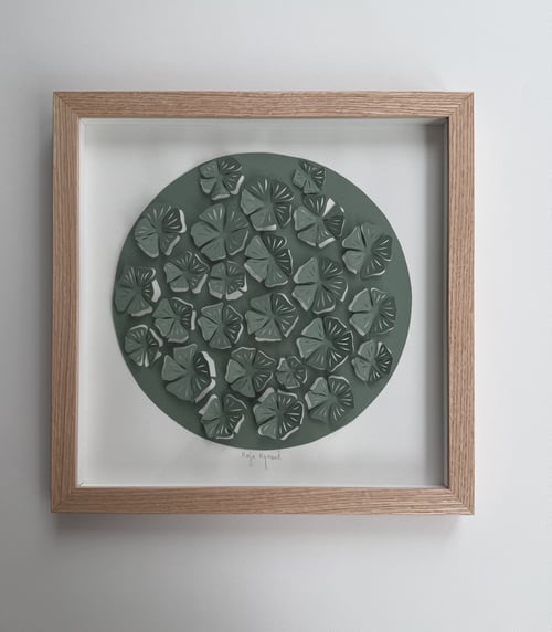 Indrammet kunstværk med grønne, udstansede og lagdelte bladformer arrangeret i en cirkel på hvid baggrund. (2)