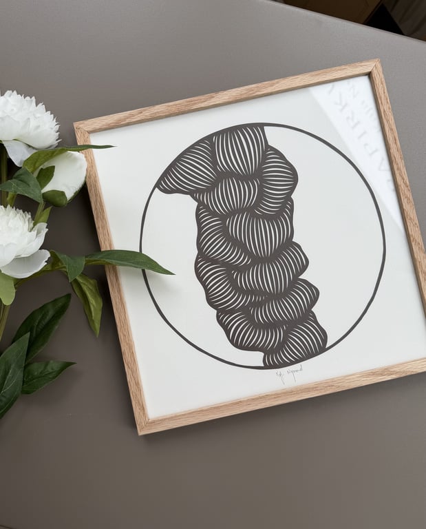 Indrammet abstrakt sort-hvid tegning med buede, parallelle linjer indenfor en cirkel på grå overflade ved siden af hvide blomster med grønne blade.