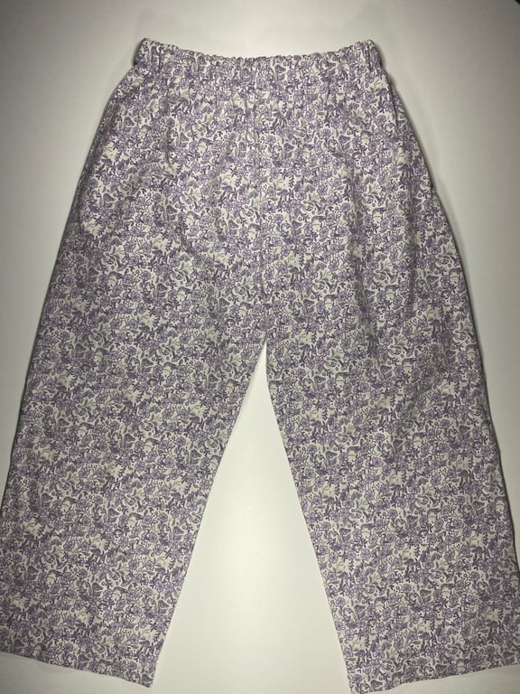Lilla og hvide blomstrede løstsiddende bukser med elastisk talje, lagt fladt på en hvid overflade.