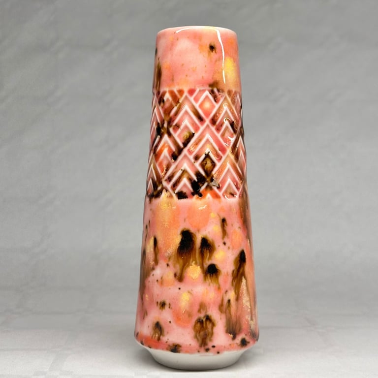 Pink og brunt glaseret keramisk vase med geometrisk mønster øverst, stående på grå baggrund.