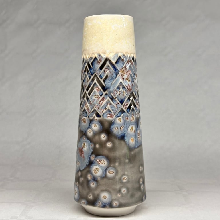 Vase med konisk form og glasur i beige, blå, grå og brune nuancer med mønster af diamanter og prikker.