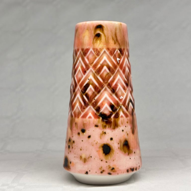 Keramisk vase i rosa og brune nuancer med mønster af trekanter og prikker.