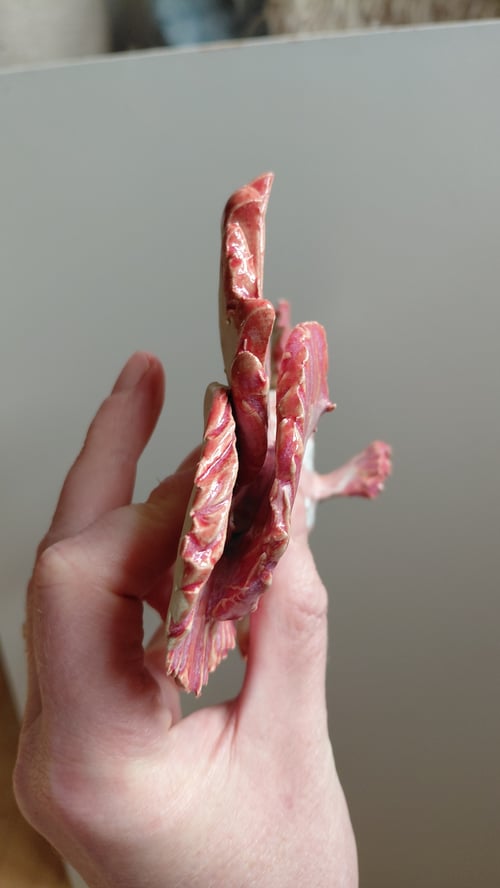 Hånd holder en skulptur af et rødt, abstrakt eller fantasidyr set fra siden. (8)