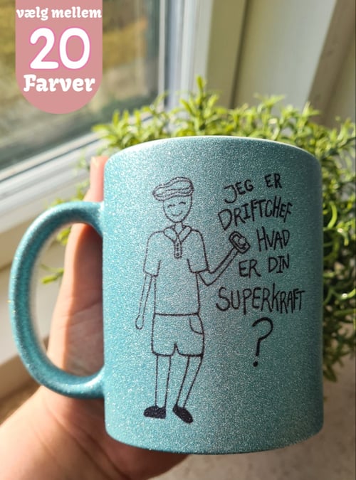 Hånd holder en glitrende blå krus med tegning af en person og teksten "Jeg er driftchef hvad er din superkraft?" samt tekst i øverste venstre hjørne, "vælg mellem 20 farver". (1)