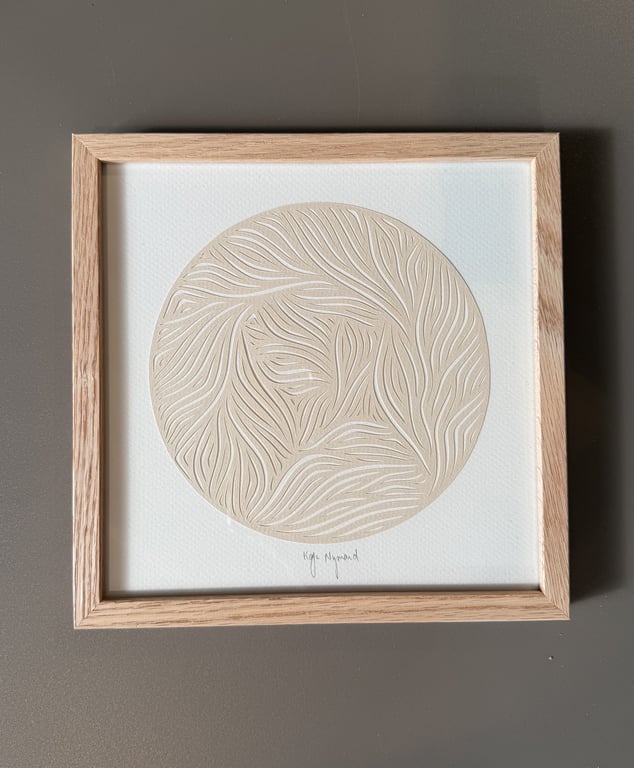 Firkantet træramme med abstrakt, rund, beige reliefkunst med bølgende linjer på hvid baggrund.