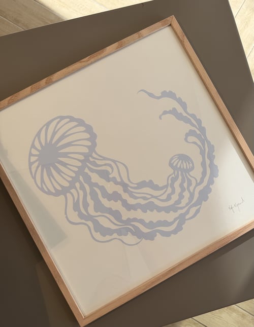 Billede af indrammet kunstprint med to grå vandmænd på cremefarvet baggrund, placeret på et gråt bord. (1)