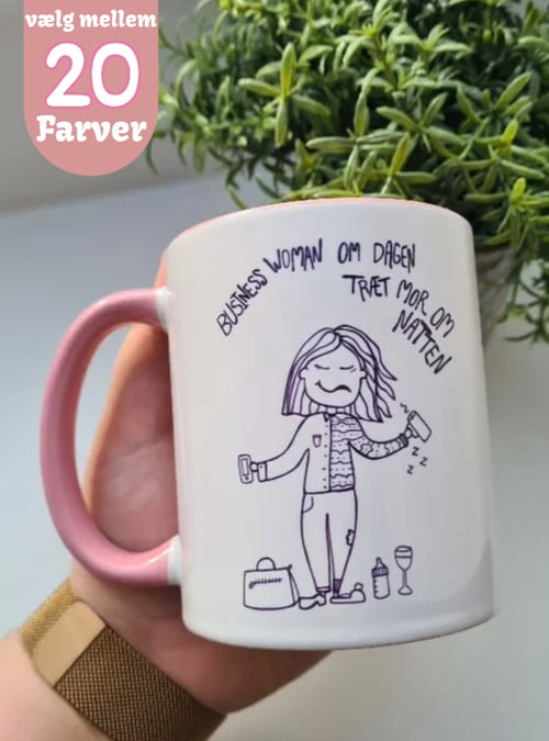 Hånd, der holder en hvid kaffekop med lyserødt håndtag og tegning af en træt kvinde med teksten "Business woman om dagen træt mor om natten", omgivet af genstande som en taske, sutteflaske og vinglas. Tekst i venstre hjørne: "vælg mellem 20 farver" (1)