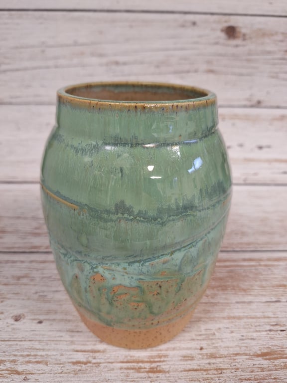 Grøn keramisk vase med glaseret overflade og brune detaljer på træbord.