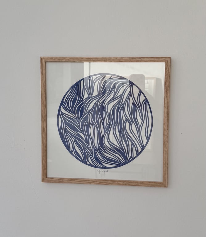 Billedramme med abstrakt kunst bestående af mørkeblå, bølgende linjer i en cirkel, på en hvid væg.