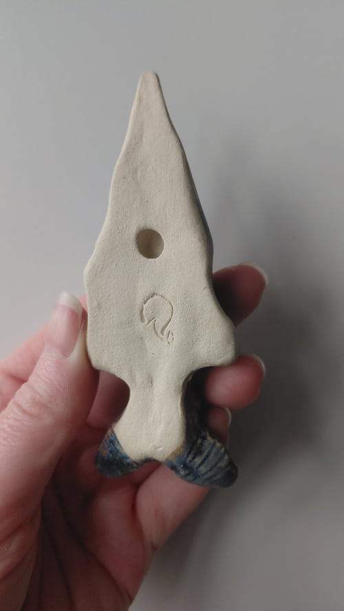 En hånd holder en hvid, trekantet keramikgenstand med et rundt hul og et indgraveret symbol midt på. (6)
