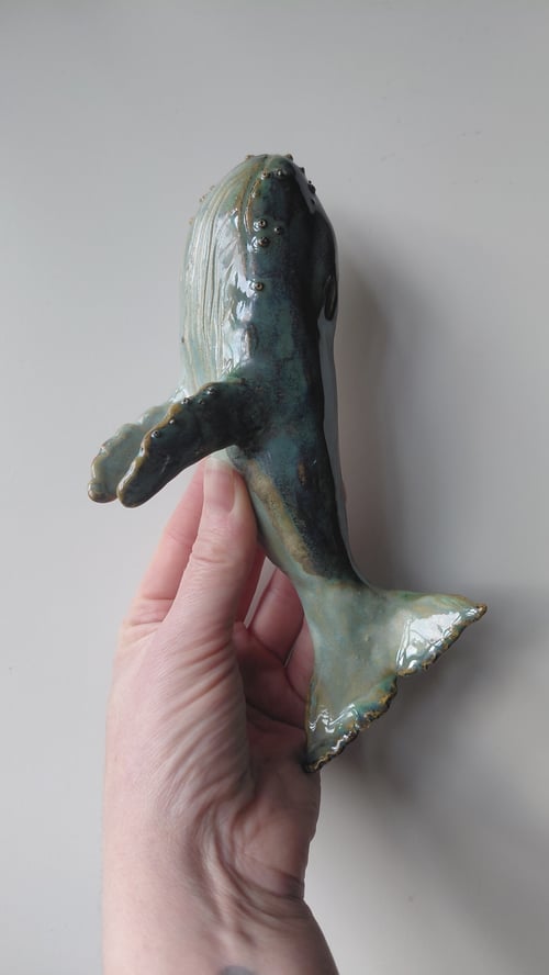 Hånd der holder en glaseret, keramisk skulptur af en hval med fin detaljer. (3)