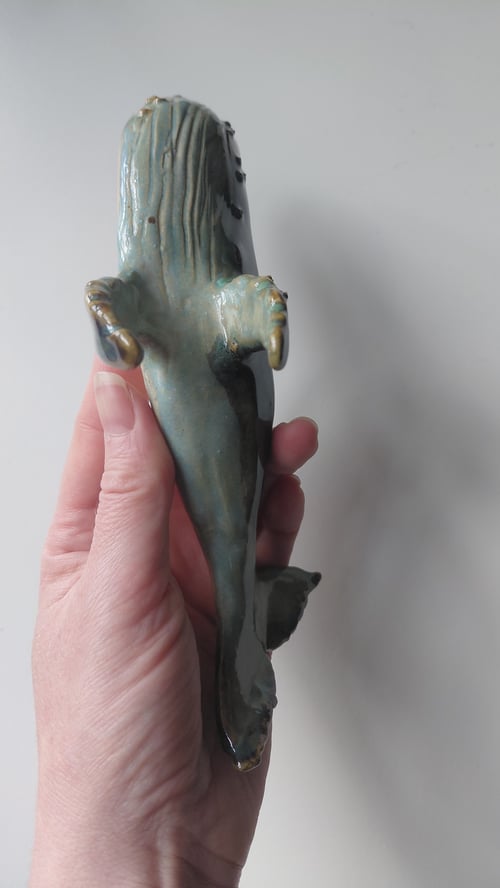 Hånd, der holder en keramisk skulptur af et havdyr, muligvis en havkylling, med grønlig og brun glasur. (7)