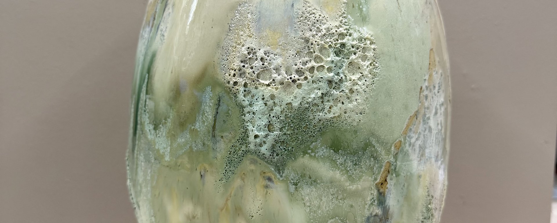 To keramiske vaser med en struktureret, glaseret overflade i grønne og beige nuancer, med et grønt blad i den ene vase.