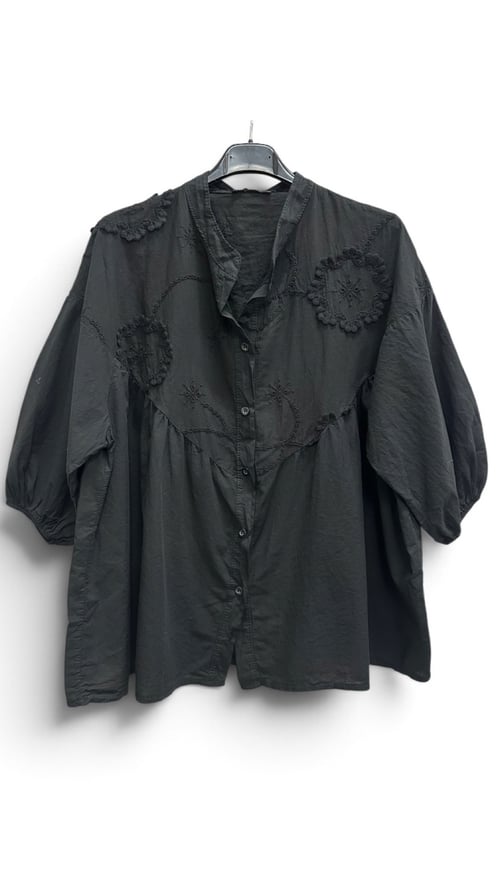 Sort bluse med knapper og broderede mønstre, hængende på en kleshenger. (3)