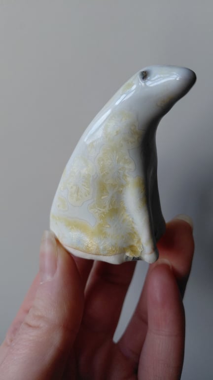 Hånd, der holder en lille, glaseret keramisk figur formet som et dyr.