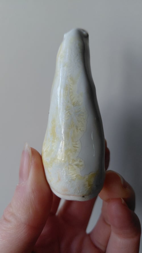 Hånd, der holder en glat, lang, hvid og beige mineralsten med blomsteragtige mønstre. (3)