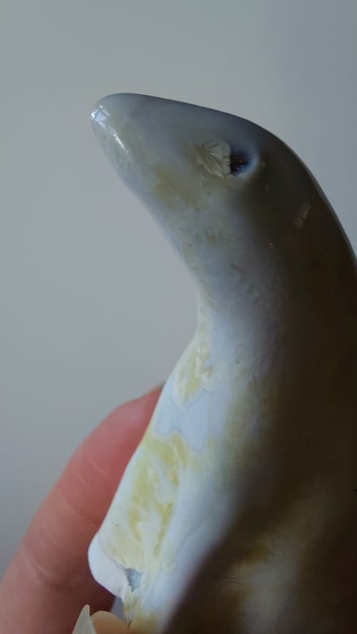 Hånd, der holder en glaseret keramikfigur af en sæl i hvid og gul farve. (6)