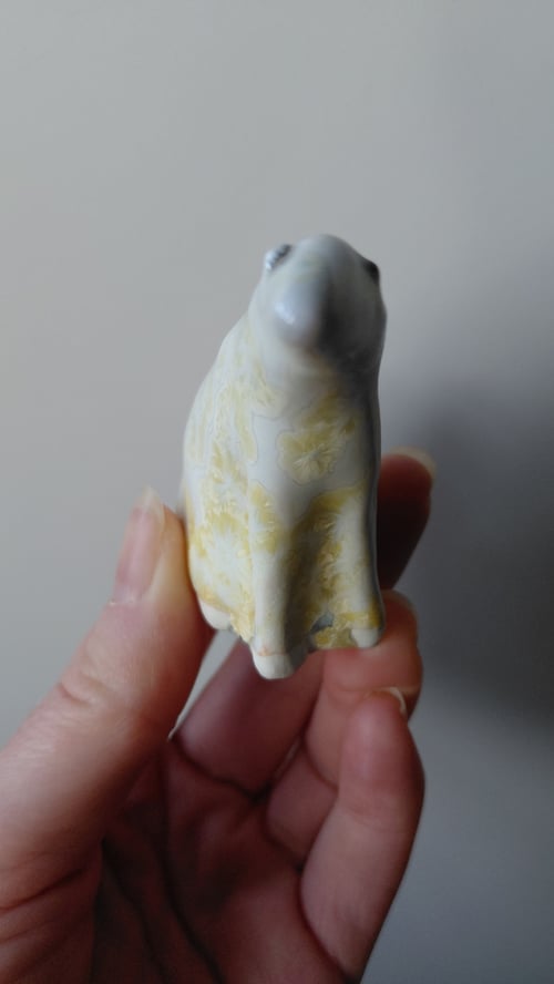 Hånd, der holder en lille keramisk figur af en hund med gul mønstret overflade. (7)