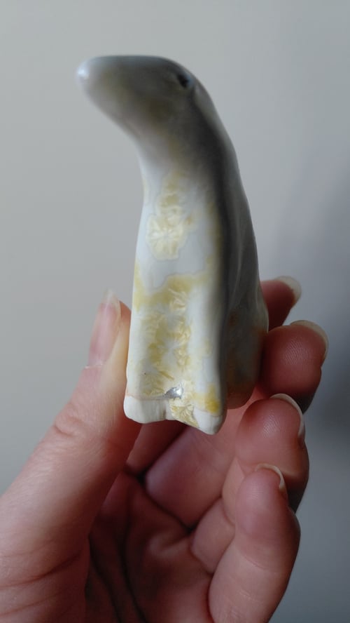 Hånd, der holder en lille, slidt hvid og beige porcelænsfigur formet som et dyr, muligvis en pingvin. (8)