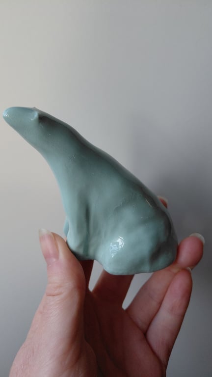 Hånd, der holder en lille, matblå keramikfigur formet som en isbjørn.