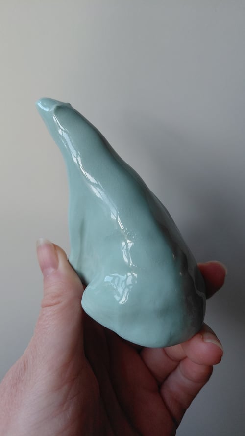 Hånd der holder en glat, lyseblå keramisk figur formet som en nøgen hånd med spidst pegefinger. (3)