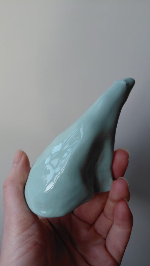 Hånd, der holder en lyseblå, glaseret keramisk figur formet som en stiliseret fugl. (5)