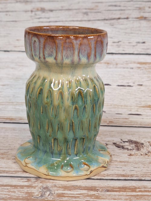 Glaseret keramisk vase med grønne, brune og beige nuancer, placeret på en træbordplade med lyst, slidt træbaggrund. (1)