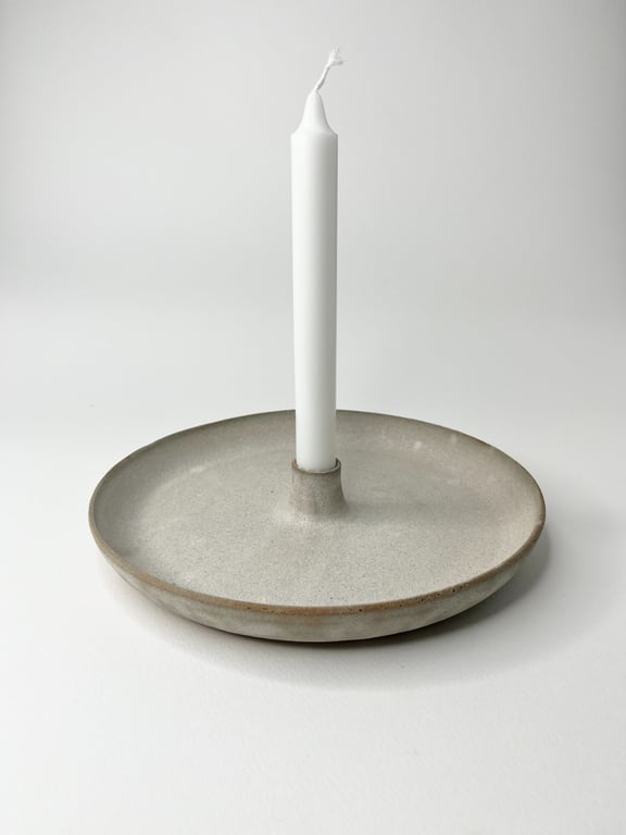 Grå keramik lysestage med hvid, ubrændt stearinlys i midten på hvid baggrund.