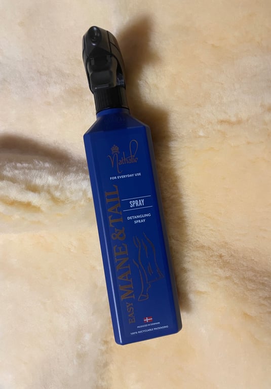 Blå flaske med Nathalie Easy Mane & Tail spray til at rede hestehår ud, placeret på en lys, blød overflade.