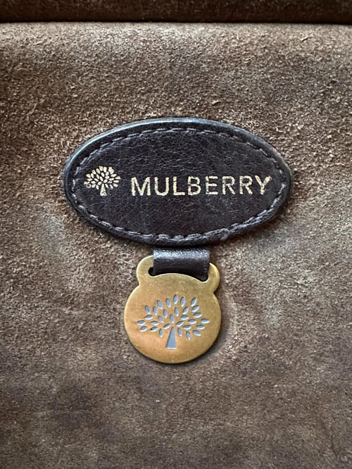 Sort læbemærke med teksten "MULBERRY" og logo, hængende på brunt ruskind. (3)