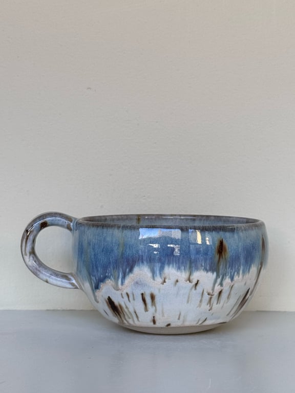 Keramisk kop med blå, hvid og brune glasurfarver, placeret på en hvid overflade.