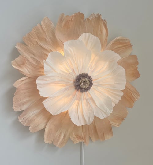 Lyskilde formet som en stor blomst med hvide og beige kronblade på en lys væg. (1)