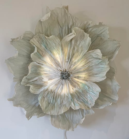 Stor, kunstnerisk vægdekoration formet som en åben blomst med flere lag af bølgede, lyse blade og blødt lys, der skinner igennem midten. (1)
