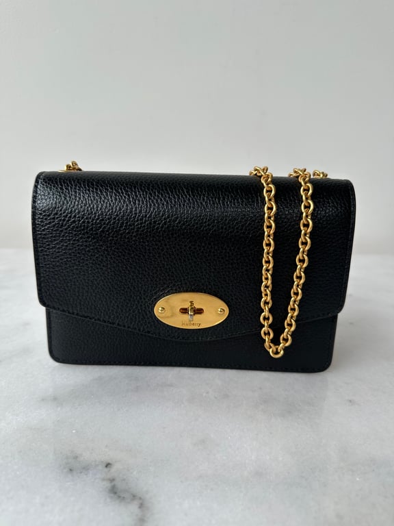 Sort lædertaske med guld farvet lås og kæde, placeret på marmorbord.