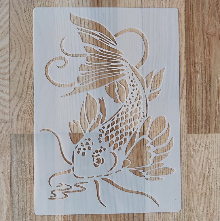 Skabelon i hvid plastik med udskåret mønster af en koi-fisk med detaljerede finner og blade, lagt på et lyst trægulv.