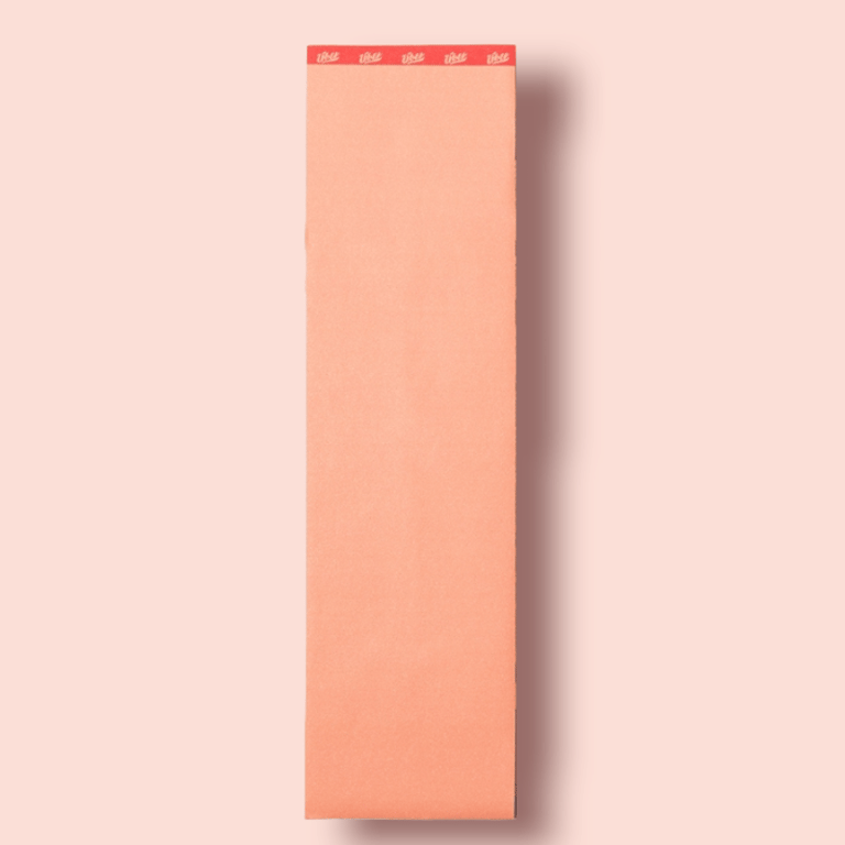 Lang, smal noteblok med orange sider og rød kant øverst med hvid tekst på lyserød baggrund.