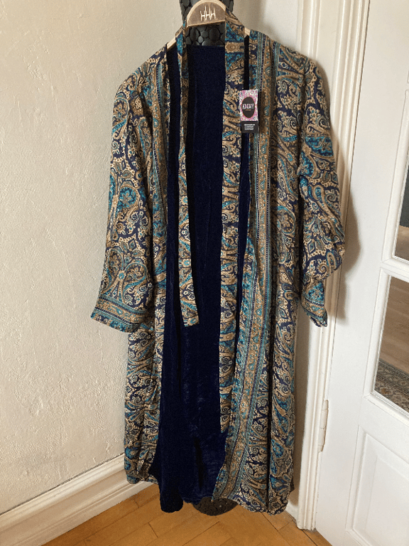 Kimono med paisleymønster i blå, beige og brune nuancer, hængende på en bøjle i et hjørne af et rum. (2)