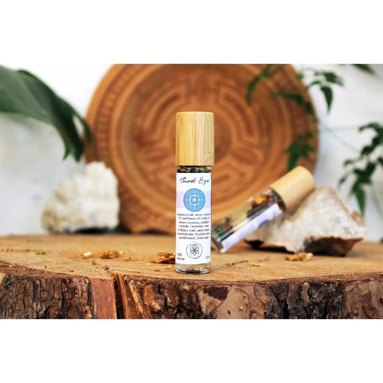 To ruller med æterisk olie med træpropper stående på et træstykke med dekorative krystaller og grønne planter i baggrunden. (4)