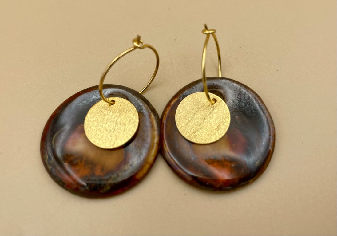 Et par øreringe med gyldne ringe og runde vedhæng i brunlig, marmorering med gyldne cirkler foran.