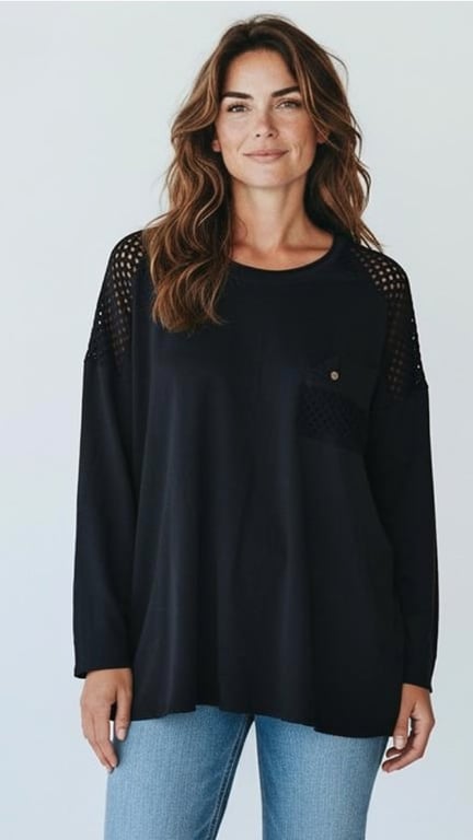 Kvinde med langt brunt hår iført en sort, langærmet bluse med netdetaljer på skuldrene og brystlomme, samt blå jeans.