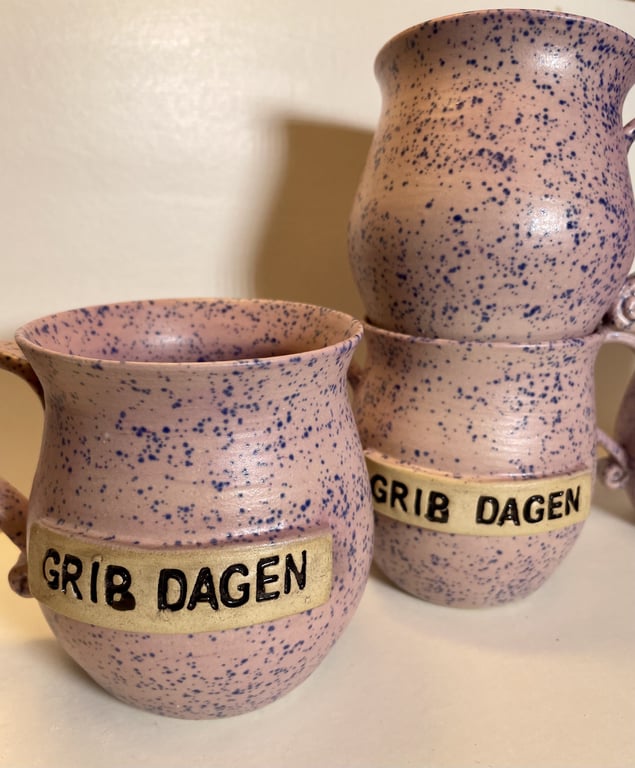 Tre lyserøde keramik krus med blåt sprøjtet mønster og teksten "GRIB DAGEN" på en cremefarvet label.