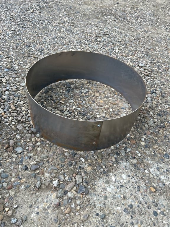 En stor metalring med nittede samlinger placeret på stenet og gruset jord.