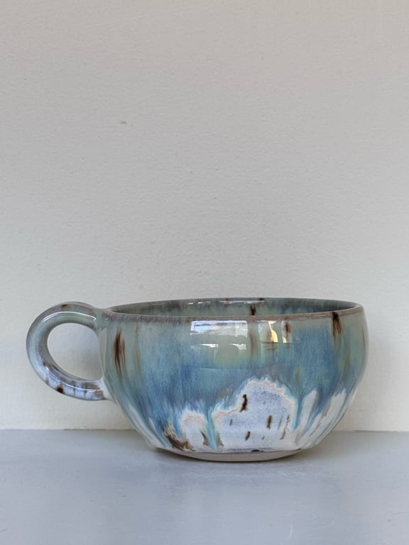 Keramikkop med blå, grønne og brune glasurstriber mod en lys baggrund.