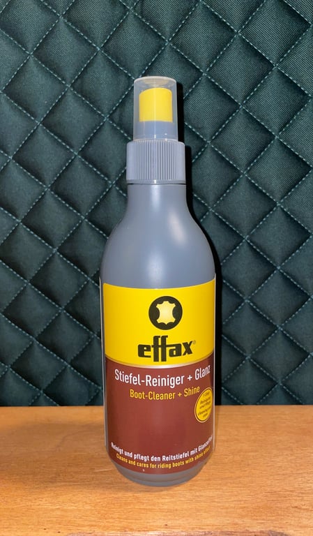Flaske med Effax Stiefel-Reiniger + Glanz støvle-rens og glans på træbord foran quiltet mørkegrønt baggrund.