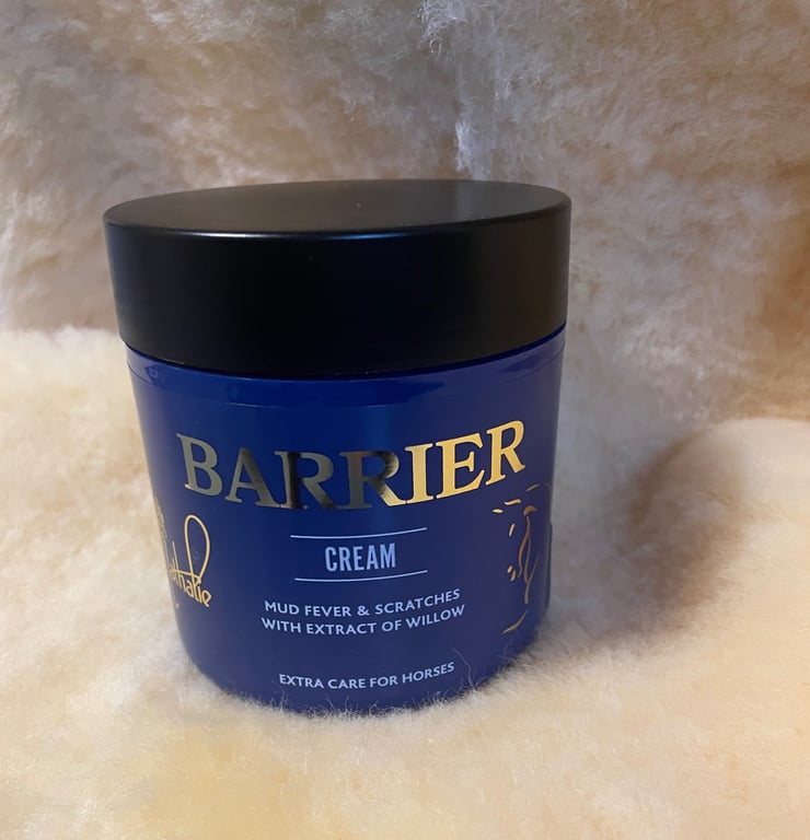 Blå krukke med sort låg af Barrier Cream, hudplejeprodukt til heste mod mudderfeber og ridser med pileekstrakt, placeret på blødt, lyst uldmateriale.