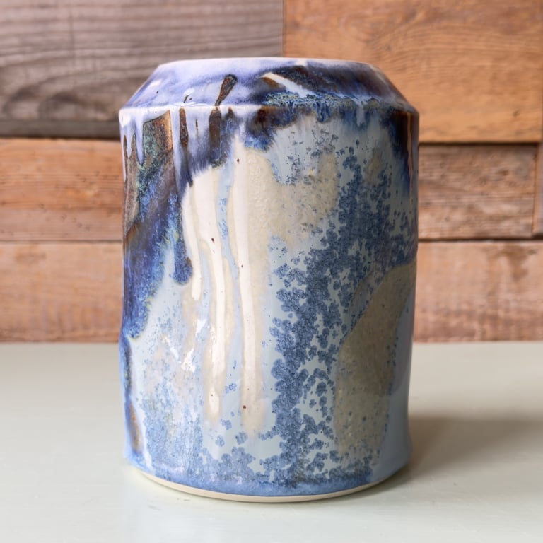 Keramisk vase med blå og hvide glasurdetaljer, stående foran en træbaggrund.