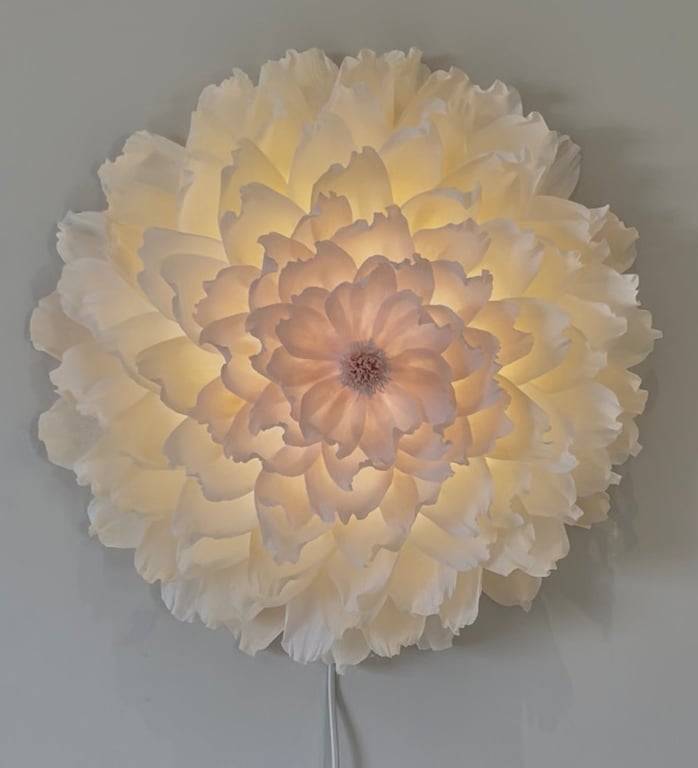 Blomstformet væglampe med bløde, hvide lagdelte skærme, der udsender varmt, diffust lys.